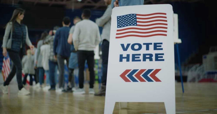 shutterstock_2454758105 People in line next to Vote Here sign