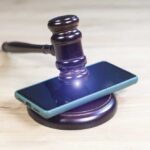 Judge’s gavel resting on a smartphone on a wooden surface