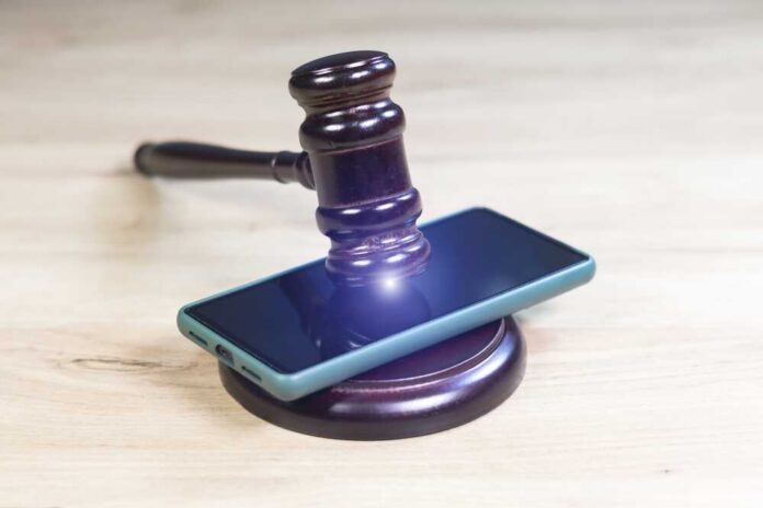 Judge,Hammer,For,Adjudication,With,Wooden,Stand,And,Smartphone,On Judge’s gavel resting on a smartphone on a wooden surface