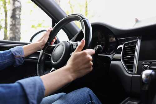 Woman,Holding,Steering,Wheel,While,Driving,Her,Car,,Closeup Hands gripping a steering wheel inside a car