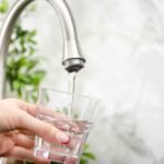 Hand filling pitcher with water from faucet.