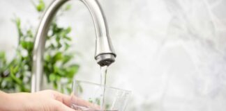 Hand filling pitcher with water from faucet.