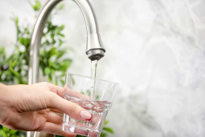 Hand filling pitcher with water from faucet.