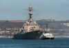 Naval destroyer escorted by a tugboat in a harbor