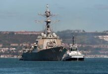 Naval destroyer escorted by a tugboat in a harbor