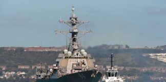 Naval destroyer escorted by a tugboat in a harbor
