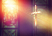 Crucifix with sunlight, stained glass window in background.