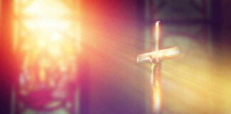 Crucifix with sunlight, stained glass window in background.