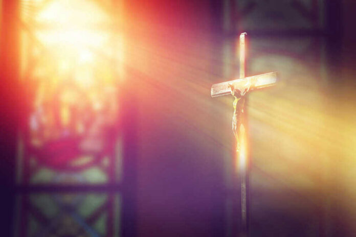 shutterstock_1034080006 Crucifix with sunlight, stained glass window in background.