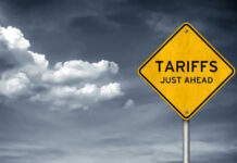 Price War Erupts — We Have The Details Yellow sign saying tariffs just ahead cloudy sky