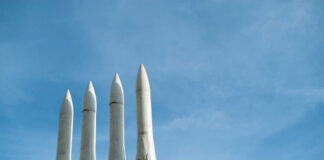 Four white missile launchers pointing upward against a blue sky
