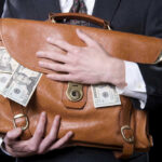 REPORT: Corruption Hits 20-Year High Person clutching leather bag with money sticking out.