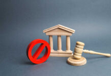 Court Reins In Trump – Tells Him ‘No’ Wooden courthouse with red prohibition symbol and judge’s gavel