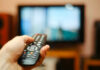 October Exit – TV Titan Walking Away Hand holding a remote control towards a TV screen.