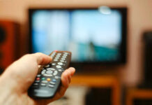 Hand holding a remote control towards a TV screen.