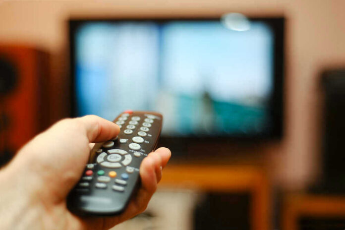 shutterstock_193018853 Hand holding a remote control towards a TV screen.