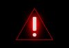 State Department Issues Travel Alert Red warning triangle with exclamation mark on black background