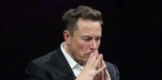Elon Musk in a suit deep in thought, black background.