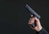 Pregnant Hostage Terror Leads To Life or Death Chase Hand holding a black semi-automatic pistol against a dark background