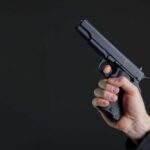 Pregnant Hostage Terror Leads To Life or Death Chase Hand holding a black semi-automatic pistol against a dark background