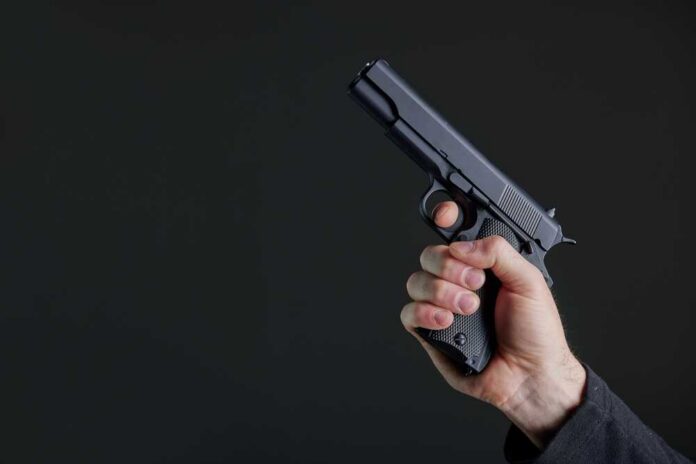 Male,Hand,Holding,A,Gun,On,Black,Background,.,A Hand holding a black semi-automatic pistol against a dark background