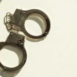 Toddler Waves Loaded Gun; Cop Arrested A pair of metallic handcuffs resting on a light surface