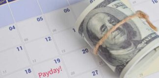 A rolled bundle of cash placed on a calendar marked with 'Payday!'