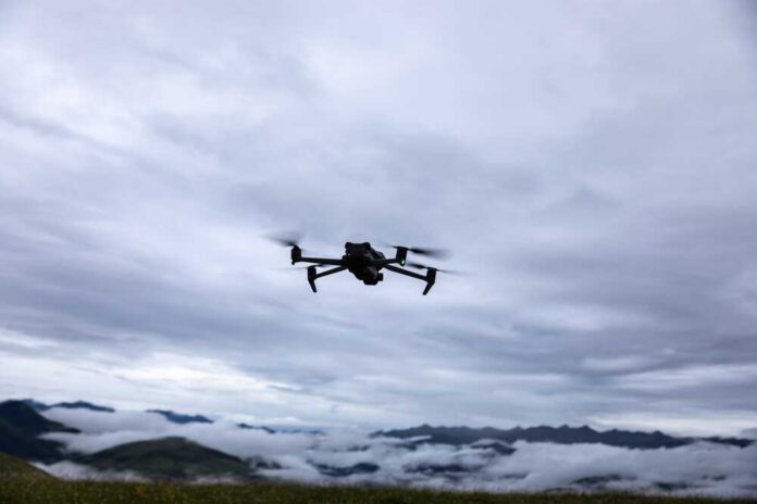 A drone flying against a cloudy sky over a mountainous landscape