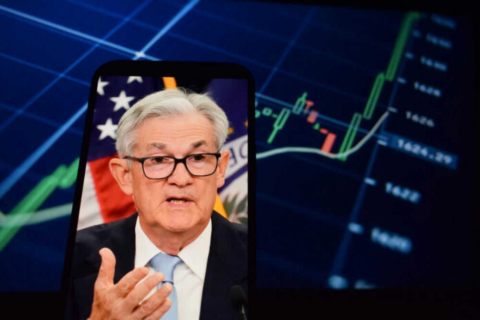 Jerome Powell speaking on a smartphone screen with stock chart in background