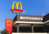 McDonald’s ‘Heist’ Menu Launched Today McDonald's restaurant exterior with drive-thru signs against blue sky