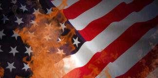 American flag partially set on fire with orange flames.