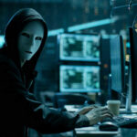 Shocking Crypto Heist By Illegal: $240M Vanishes Person in hoodie and mask using computer, multiple screens.