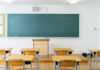 Empty classroom with desks, chalkboard, and clock.