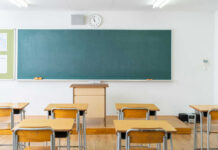 Empty classroom with desks, chalkboard, and clock.