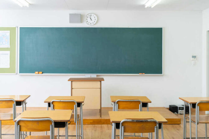 Empty classroom with desks, chalkboard, and clock.