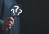 Missing Aviator Clue Found? Hand holding magnifying glass with question marks.