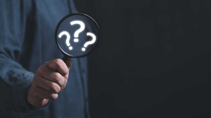 shutterstock_2278136667 Hand holding magnifying glass with question marks.