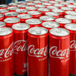 Coca-Cola’s Flavor Bomb Lands 2027 Coca-Cola cans stacked on a surface.