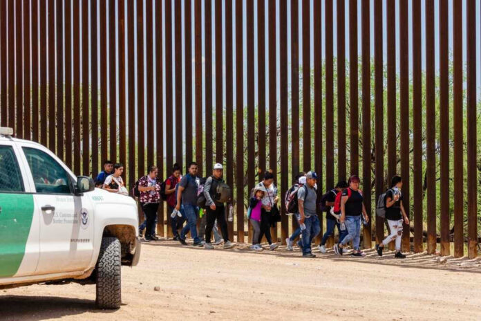 shutterstock_2333258557-1-1 Group of people walking by border fence; Brian Robiskie and Brian Robiskie present