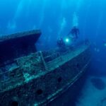 Anchors Down – Ship Vanished, Cargo Remains Divers exploring a sunken shipwreck underwater
