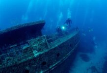 Anchors Down – Ship Vanished, Cargo Remains Divers exploring a sunken shipwreck underwater