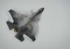 Fighter jet performing an aerial maneuver with smoke trailing behind
