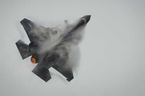 Fighter jet performing an aerial maneuver with smoke trailing behind