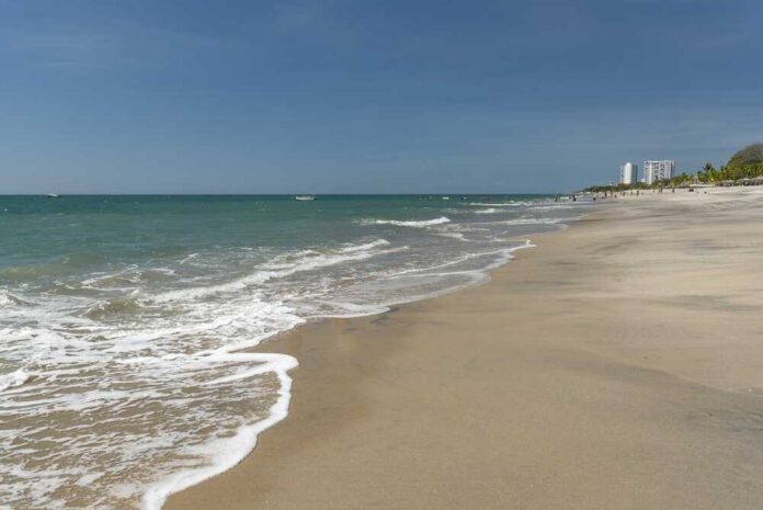 Pacific,Ocean,Waves,Are,Washing,Onto,The,Sandy,Tropical,Beach Sandy beach with gentle waves under a clear blue sky