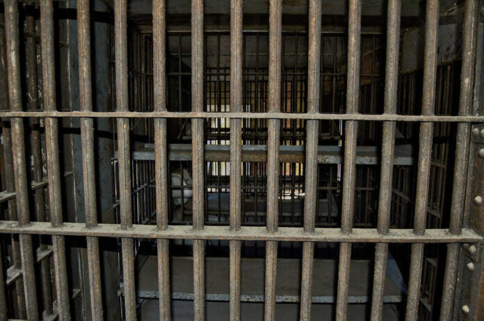 shutterstock_747318307 Empty, rusty barred jail cell with metal bunks.